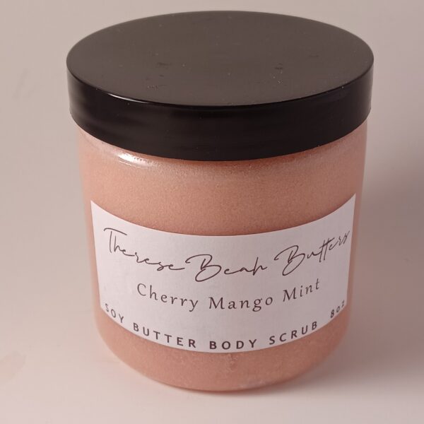 Clear jar with black lid. ThereseBeah Butters logo in fancy script. Cherry Mango Mint soy butter scrub detailing fragrance written in script detailing 8 ounce product content. Scrub is a dark pink color.